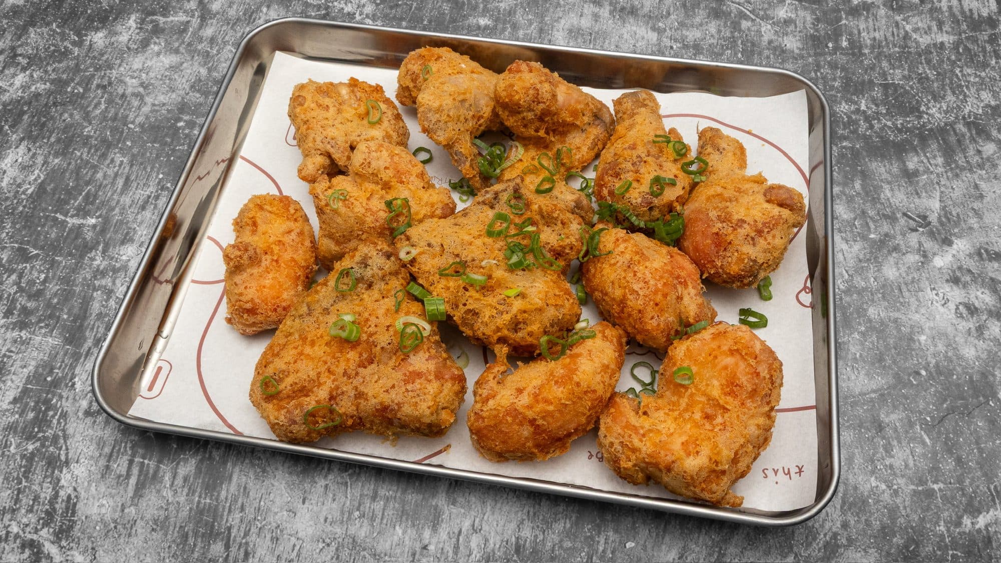 A tray of triple-fried Korean fried chicken, the crust craggy and golden, finished with spring onion on INYUN paper
